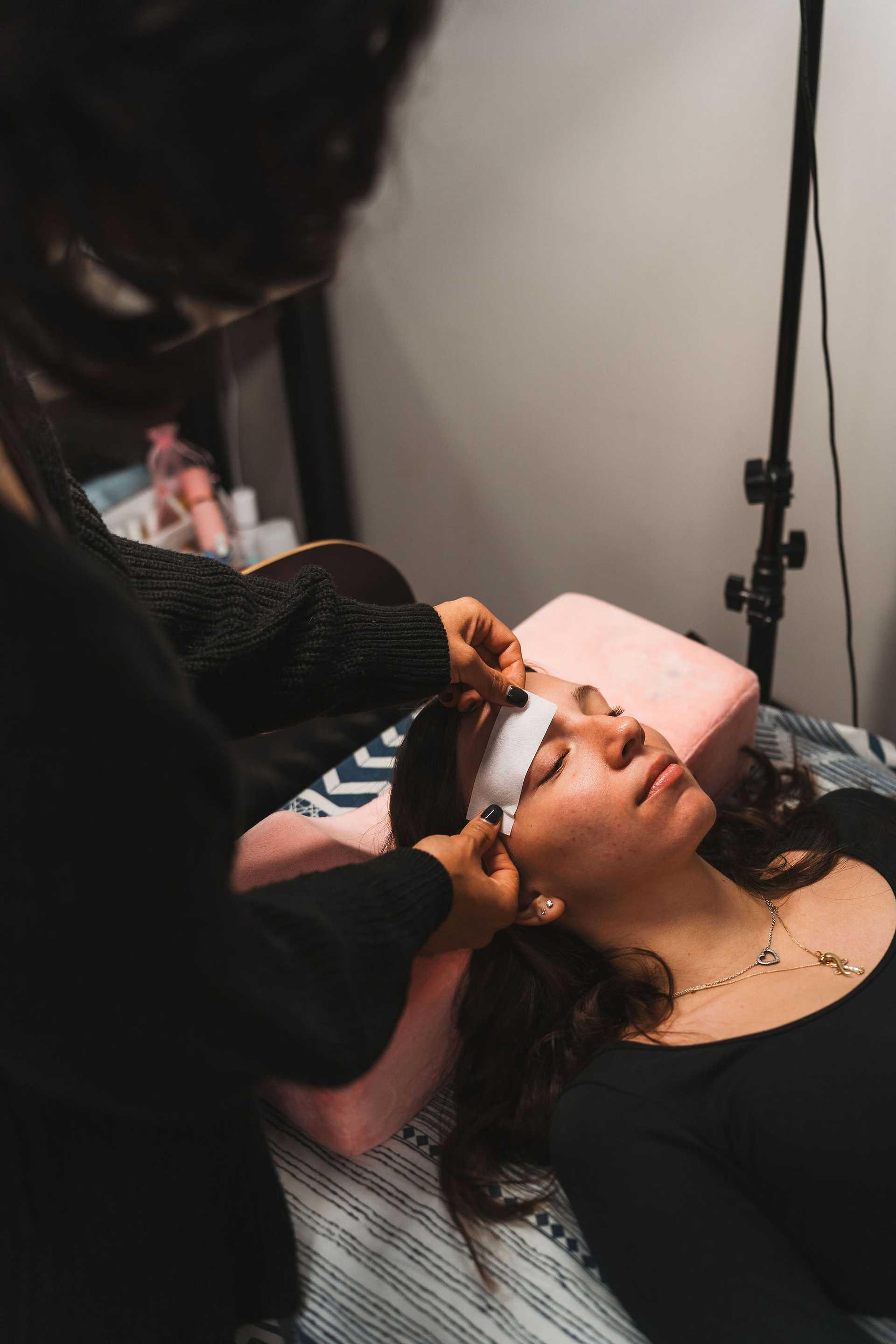 Woman receiving a forehead skincare treatment, lying on a bed with a pink cushion.