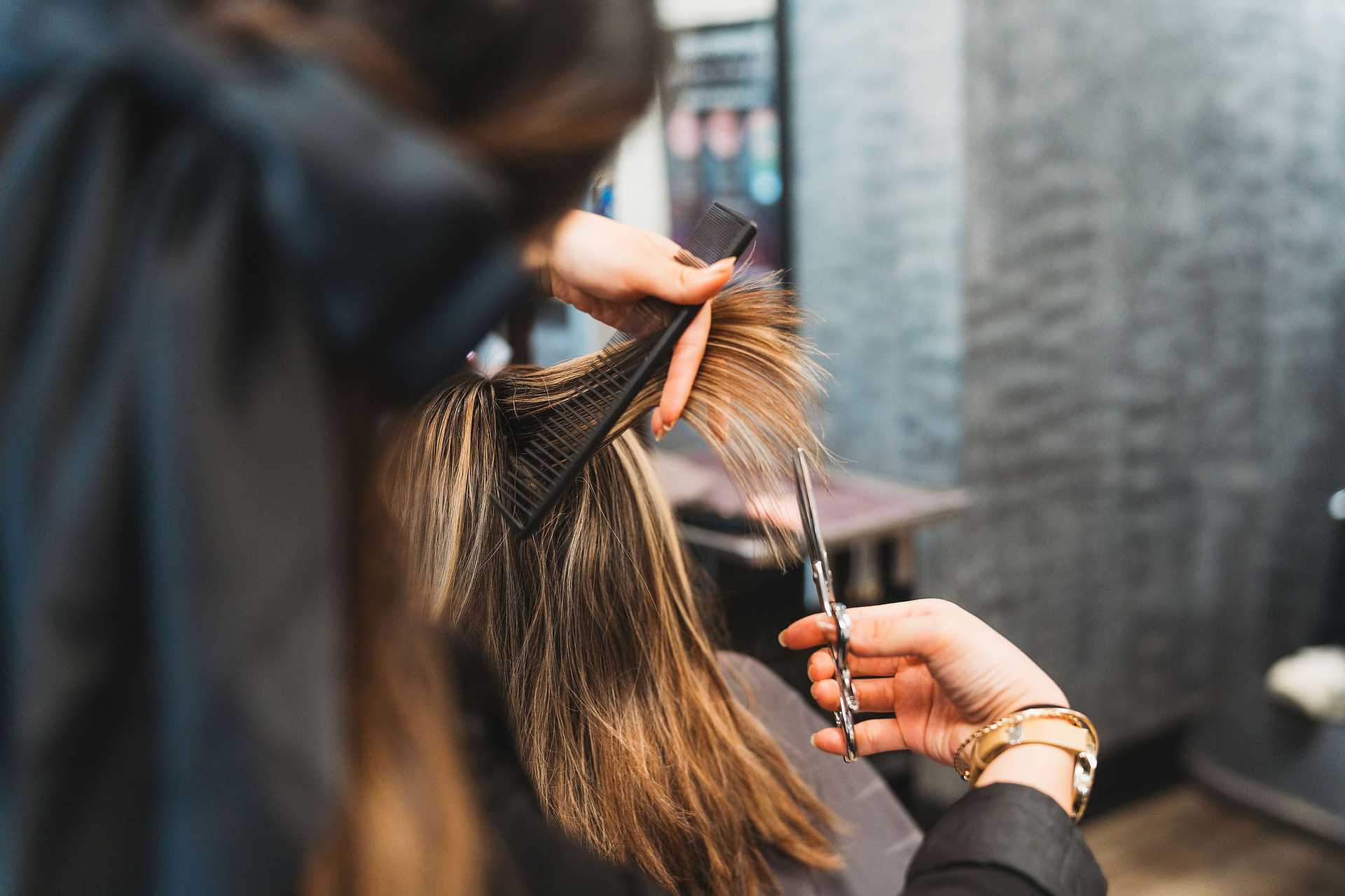 Person getting a haircut with scissors and comb in a salon.